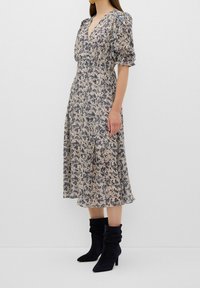 Robe midi fleurie avec manches bouffantes, fond crème, imprimé bleu marine, encolure en V et jupe fluide. Associée à des bottines sombres et décontractées.