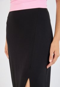 Schwarzer Maxikleid aus Jersey mit einem seitlichen Schlitz, glatter Textur und einem elastischen Taillenbund, kombiniert mit einem hellrosa ärmellosen Oberteil.