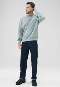 Grå sweatshirt med en tekstureret overflade, parret med mørkeblå jeans og sorte støvler. Outfittet har et afslappet design med en løs pasform.
