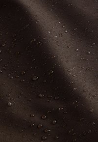 Tessuto marrone scuro resistente all'acqua con una superficie liscia, caratterizzato da gocce d'acqua sparse che creano una superficie lucida e riflettente.