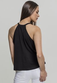Svart ermeløs topp med høy hals og racerback-design. Mykt stoff med en avslappet passform, bakhemmet er litt lengre enn foran.