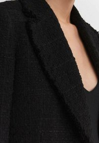 Schwarze strukturierte Blazerjacke mit Reverskragen, aus einem gewebten Stoff gefertigt. Verfügt über eine figurbetonte Silhouette und dezente Details.