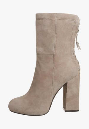 Botte de cheville en suède beige avec un talon empilé, texture lisse, détail de lacets sur le côté et bout rond. Design élégant mais simple.