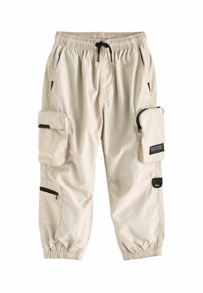 Pantalons cargo beiges avec taille élastique, plusieurs poches, y compris une poche latérale zippée, et des poignets froncés aux chevilles.