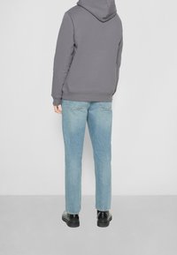 Felpa grigia con tasca a marsupio, jeans dritti blu sbiaditi e stivali neri alla caviglia, visti da dietro.