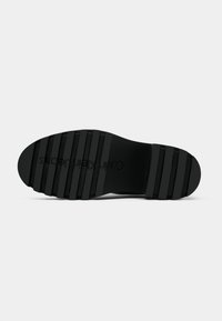 Black shoe sole with deep horizontal grooves and "Calvin Klein Jeans" logo embossed in the center, viewed from below.