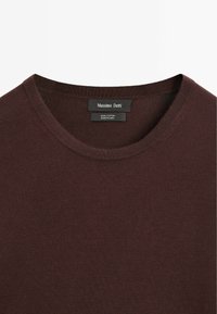 T-shirt in cotone di un ricco color borgogna con scollo a costine. Presenta un'etichetta del marchio al collo e una texture liscia e uniforme.