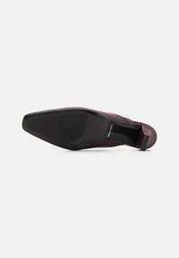 Burgundi slip-on cipő sima felülettel, hegyes orral, vékony sarokkal és fekete gumitalppal. Kényelmes, párnázott sarokkal rendelkezik.