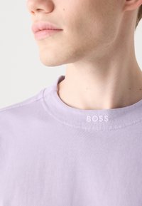 Levandulová košile s krátkým rukávem vyrobená z měkké tkaniny. Má kulatý výstřih a malé vyšívané logo "BOSS" na límci.