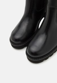 Bottines en cuir noir avec une finition lisse, bout arrondi et semelle en caoutchouc présentant des détails texturés le long du bord.