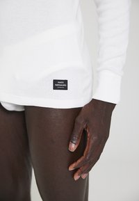 Hvid langærmet skjorte lavet af bomuld med en tekstureret finish. Har et lille sort mærke med "MADS NØRGAARD" tekst i kanten.