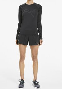 Maglietta atletica nera a maniche lunghe con un discreto logo Puma grigio, abbinata a pantaloni corti neri e scarpe da corsa grigie con accenti arcobaleno.
