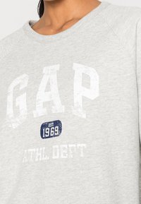 Sweatshirt gris avec un col ras du cou, des manches raglan et une impression blanche usée avec le design "GAP ATHL DEPT EST. 1969".