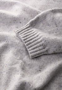 Szary sweter o dzianinowym splocie z prążkowanymi mankietami i rozproszonymi kropeczkami koloru. Miękka tekstura, z luźnym krojem i delikatnym opadaniem.