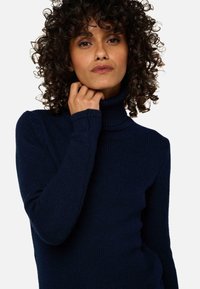 Pull en laine marine à col montant, présentant une texture côtelée et un design ajusté, avec des manches longues et un col haut.