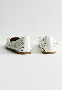 Ballerine bianche realizzate in pelle perforata, con fori a forma di fiore, un profilo basso e una suola marrone in contrasto.