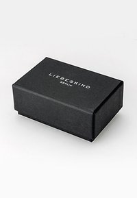 Zwarte rechthoekige doos met een getextureerd stoffen oppervlak, met de hooggedrukte merknaam "LIEBESKIND" in witte letters op de bovenkant.