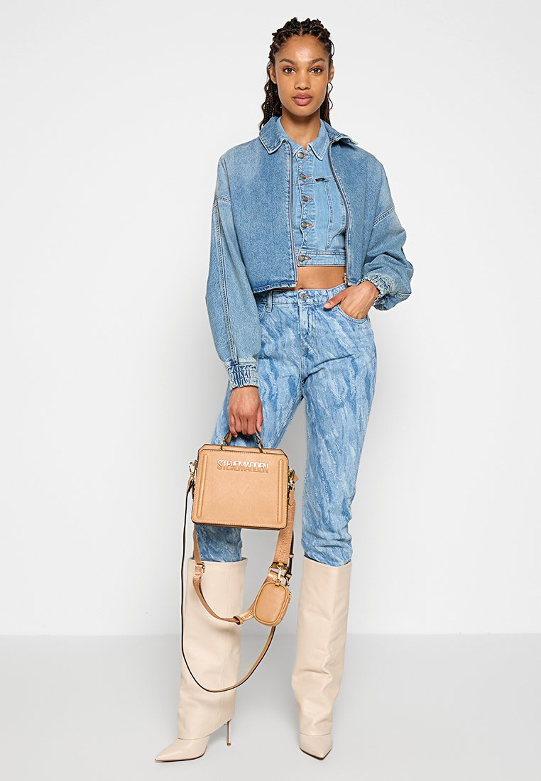 Jasnoniebieska kurtka dżinsowa i krótki top, w połączeniu z wzorzystymi niebieskimi dżinsami, beżowymi kozakami za kolano oraz torebką w kolorze brązowym z logo.