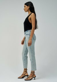 Top negro sin mangas, jeans de tiro alto en azul claro y sandalias de tacón negro con tiras. Tejido suave, diseño ajustado y pierna acampanada.