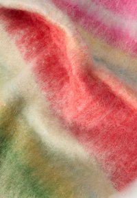 Tissu doux et pelucheux avec des rayures dégradées en tons rouge, rose, crème et vert, montrant une texture détaillée et des plis délicats.