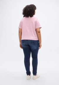 Ροζ ανοιχτό ροζ βαμβακερό T-shirt με κοντά μανίκια, σε συνδυασμό με στενά σκούρα μπλε τζιν και μπεζ αθλητικά παπούτσια, από πίσω.