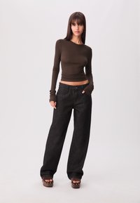 Dunkel gewaschene weite Jeans kombiniert mit einem eng anliegenden braunen Langarmshirt mit Daumenlöchern. Das Model trägt braune Plateausandalen.