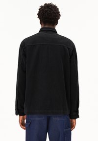 Zwart corduroy jack met een kraag, lange mouwen en een rechte snit. Heeft verticale ribbels en een relaxte pasvorm.