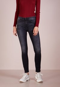 Jeans ajustados de lavado oscuro con una cintura de media altura, diseño de cinco bolsillos y un desgaste sutil. Combinados con una blusa de manga larga burdeos de canalé y zapatillas blancas.