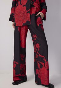 Schwarzer Stoff mit auffälligem roten Blumenmuster, bestehend aus weit geschnittenen, locker sitzenden Hosen und einem passenden Hemd mit Knopfleiste. Glatte Textur.