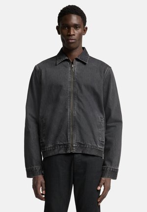 Zwarte denimjas met een rits aan de voorkant, puntkraag en twee zijzakken. De stof heeft een lichte textuur en een klassieke pasvorm.