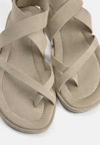 Beige sandalen met kruislings ontwerp, gemaakt van een zacht suède-achtig materiaal. Dunne banden en een platte zool met stiksel details.