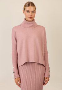 Rosa Rollkragenpullover mit gerippten Ärmeln und dekorativen Knöpfen an den Bündchen, aus weichem Strickmaterial gefertigt, mit lässiger Passform.