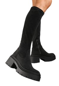 Bottes noires en daim montantes jusqu'au genou avec une semelle épaisse et une fermeture éclair sur le côté, présentant une texture lisse et un design à bout rond.