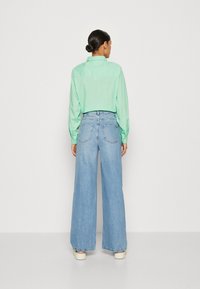 Camisa de botón en verde menta combinada con pantalones vaqueros de pierna ancha en azul claro, que cuentan con bolsillos traseros y un corte relajado.