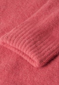 Pull en tricot dans un matériau rose doux et duveteux, avec un revers roulé à texture côtelée, mettant en avant un design confortable et décontracté.