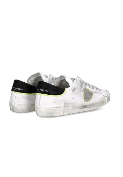 Zapatillas deportivas de cuero blanco con un acabado ligeramente desgastado, acentos en amarillo neón, detalles perforados y pestañas en negro en el talón. Suelas de goma.