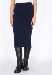 Navy blauwe gebreide midi-rok met geribbelde textuur en elastische tailleband, gecombineerd met glanzende zwarte kniehoge laarzen met gespaccenten.