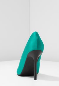 Tyrkysová saténová lodička na vysokém podpatku s špičatou špičkou a černým stejnokrojovým podpatkem, s hladkou texturou a detaily švů.
