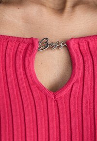 Top rosa a costine con scollatura a chiave, dotato di un'emblema argento "Boss" come accento decorativo. Texture liscia e design aderente.