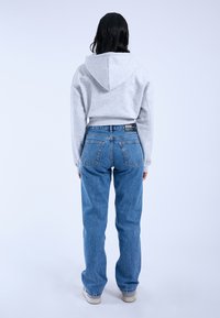 Gray cropped hoodie with hood, paired with loose-fit blue denim jeans featuring a slightly faded texture and back pockets.