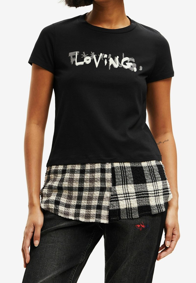 T-shirt nera in cotone con la scritta "Loving" in lettere bianche consumate, abbinata a un pannello a quadri nero e bianco strutturato sull'orlo.