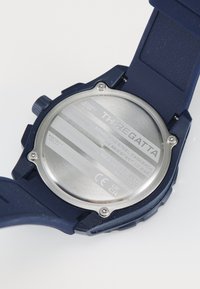 Arrière d'une montre de sport bleue montrant un boîtier arrière en acier inoxydable avec la marque "TH-REGATTA" et des détails sur la résistance à l'eau.