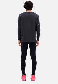 Schwarzes langärmliges Sporttop, enganliegende schwarze Leggings und pinke Laufschuhe. Strukturierter Stoff mit reflektierenden Akzenten und einem aerodynamischen Design.