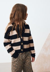 Stribet cardigan i sort og beige med ribstrikket tekstur og fire brune knapper; kombineret med brune bukser med leopardprint.