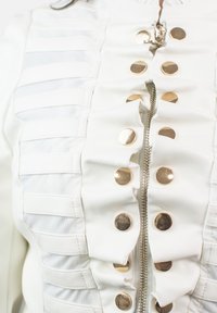Chaqueta de cuero blanca con volantes en el frente, textura de rayas horizontales, botones de hardware dorado y una cremallera central.