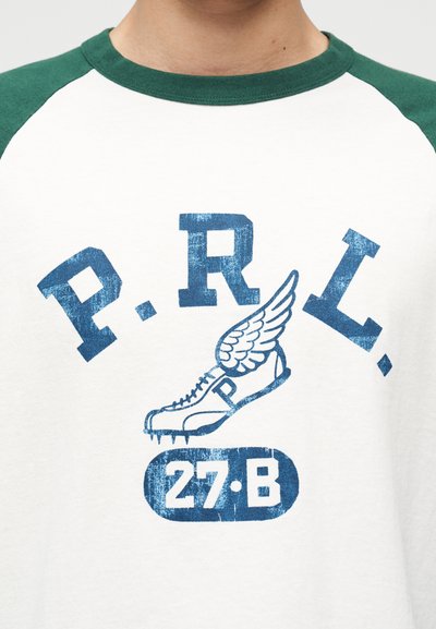 Λευκό μπλουζάκι με πράσινο γιακά και μανίκια, με μπλε κείμενο "P.R.L." πάνω από ένα φτερωτό δρομικό παπούτσι και "27·B" από κάτω.