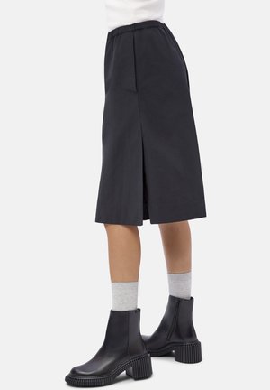 Mid-length black skirt with a back slit, worn with light gray socks and black ankle boots featuring chunky textured soles.