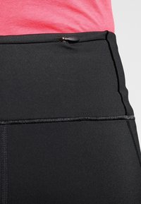 Czarne legginsy high-waisted wykonane są z gładkiego, elastycznego materiału z płaskimi szwami i małym detalem w postaci zamka na wysokości talii, co zapewnia bezpieczne przechowywanie.