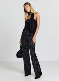 Schwarzes, schulterfreies Oberteil aus Satin, kombiniert mit schwarzen, ausgestellten Hosen mit Pailletten. Accessoires umfassen eine kleine schwarze Tasche und einen langen Stoffschal.