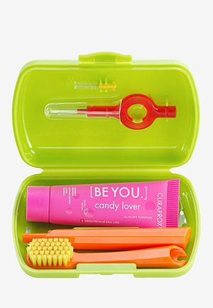 Valigetta da viaggio verde contenente dentifricio rosa, uno strumento dentale rosso, uno spazzolino arancione e dispositivi di pulizia con colori coordinati.